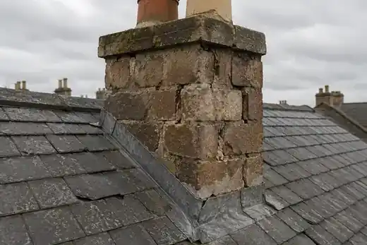 Weathered chimney stack and lead flashing on a slate roof